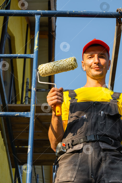 Скачать Строитель с роликом, стоящий на фасадных лесах, заканчивающий внешний ремонт, обустройство дома, услуги разнорабочего, консультационный звонок, набор инструментов, оборудование, проект. фотосток Ozero