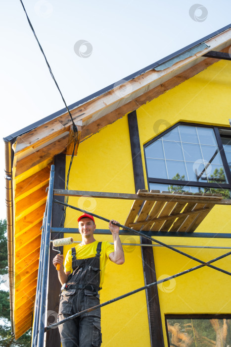 Скачать Молодой мастер на все руки в красной шапочке с пилой в руках на стройплощадке, строительство деревянных домов, плотницкие работы, навыки "сделай сам", частный ремонтный бизнес на дому. фотосток Ozero