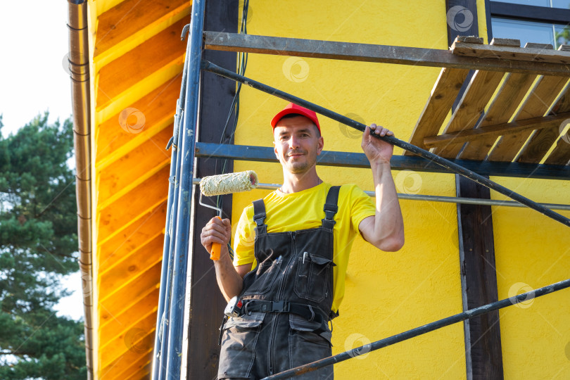 Скачать Портрет строителя в красной шапочке с нивелиром, проект дома для самостоятельной постройки, частный бизнес разнорабочего, внешний ремонт, навыки "сделай сам". фотосток Ozero
