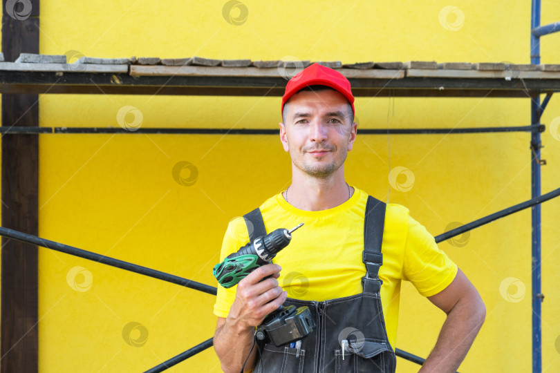 Скачать Строитель с электродрелью, строительная площадка для дома, ремонт своими руками, частный клиент, удобный набор инструментов, выезд в сервисную службу на дом, столярные работы и ремонт. фотосток Ozero