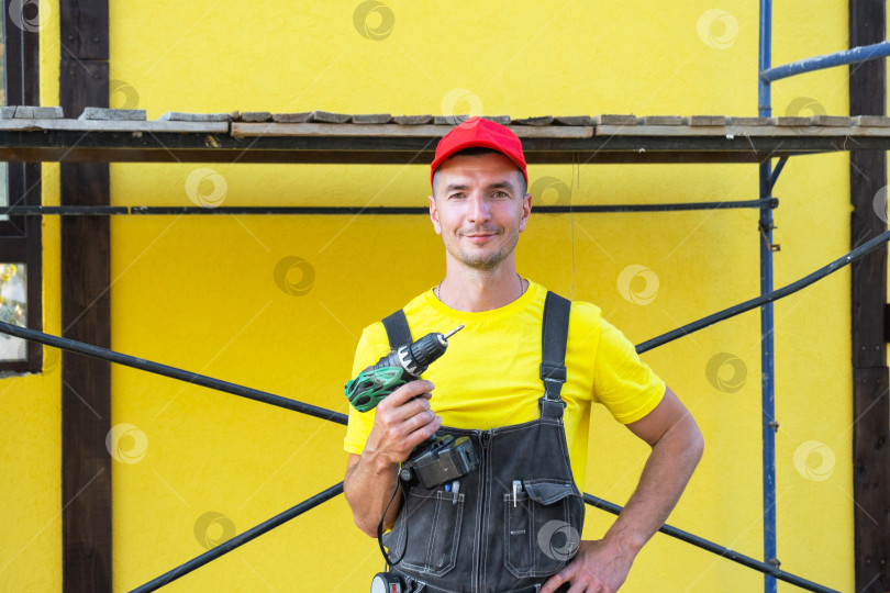 Скачать Строитель в красной шапочке с электродрелью в руках, работы по техническому обслуживанию, обустройство дома, услуги частного мастера, выезд к клиенту на объект, навыки самостоятельного строительства. фотосток Ozero