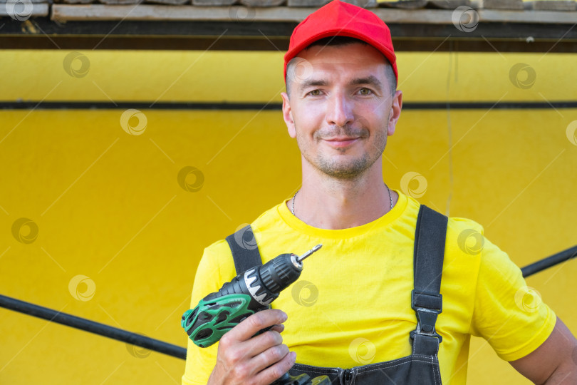 Скачать Портрет мастера на все руки в желтой футболке, держащего в руках электрическую дрель, частный ремонтный бизнес, ремонт на месте клиента, строительство дома, настройка инструмента своими руками. фотосток Ozero