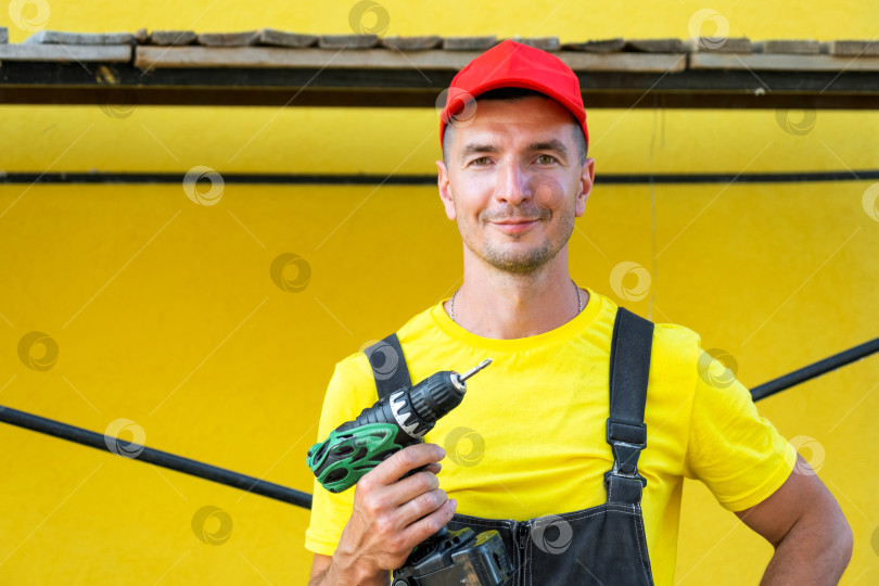 Скачать Строитель с аккумуляторной дрелью и набором инструментов, стоящий у строящегося дома, ремонт на дому, профессиональный подрядчик, навыки самостоятельного совершенствования. фотосток Ozero