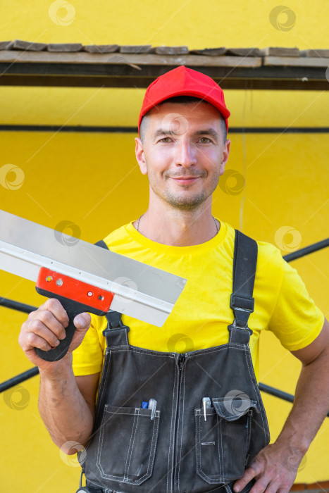 Скачать Мастер на все руки в желтом, с большим шпателем в руках, ремонт на дому, частный строительный бизнес, обустройство дома своими руками, профессиональная настройка инструмента. фотосток Ozero