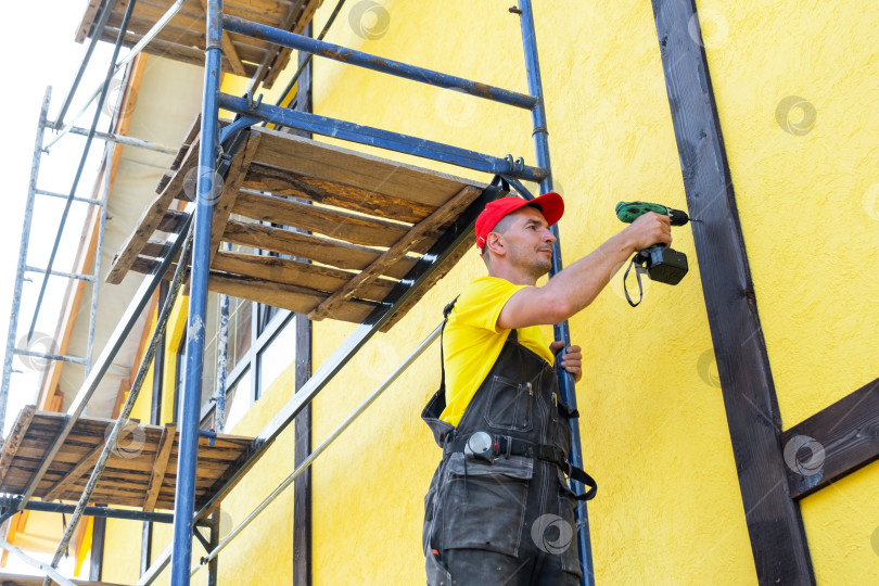 Скачать Строитель с помощью отвертки монтирует фасадную древесину, декоративный стиль фахверк, внешний вид дома, архитектурную облицовку, ремонт, услуги по благоустройству частных домов. фотосток Ozero