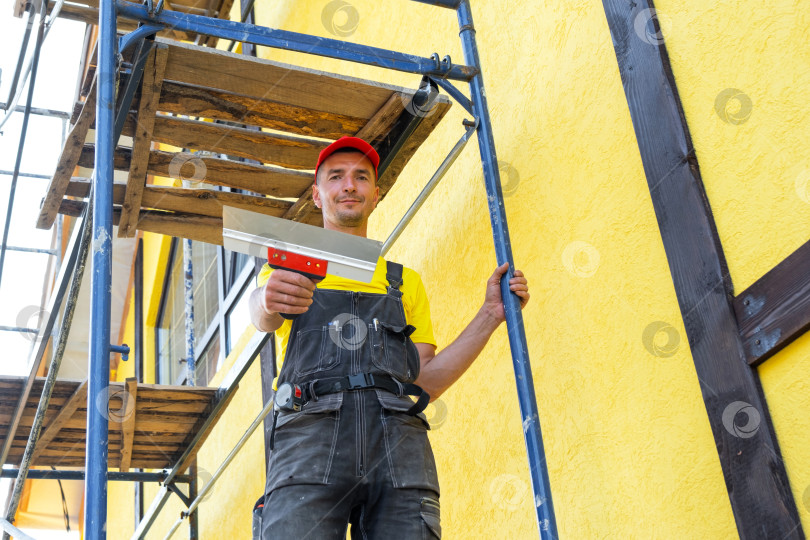 Скачать Штукатур с кельмой на фасаде, оштукатуривание и выравнивание наружных стен, выравнивание поверхности, декоративная отделка, частный бизнес, профессиональная подготовка стен. фотосток Ozero