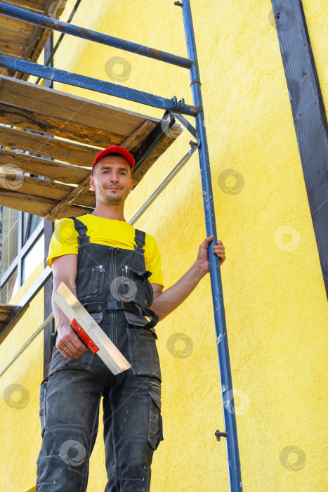 Скачать Мастер-штукатур с кельмой на строительных лесах, фасадные работы, нанесение и выравнивание состава, наружная отделка, частный ремонтный бизнес, благоустройство дома. фотосток Ozero