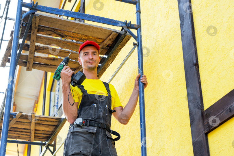 Скачать Фасадный мастер с отверткой на строительных лесах, наружный монтаж и закрепление, установка элементов, частный строительный бизнес, профессиональный строитель. фотосток Ozero