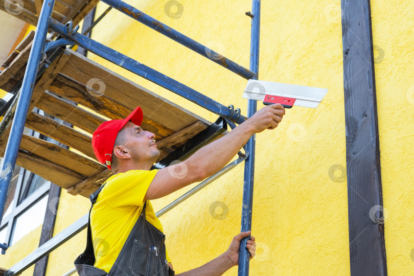 Скачать Штукатурный подрядчик на фасаде, использующий шпатель для тонкой отделки стен, выравнивания, реставрации, декоративных и подготовительных работ, ремонт частного дома. фотосток Ozero