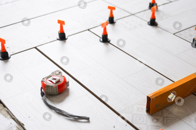 Скачать Крупный план системы выравнивания плитки во время укладки плитки на пол, прокладок и измерительной ленты, ремонтных работ дома, точной укладки керамического напольного покрытия. фотосток Ozero