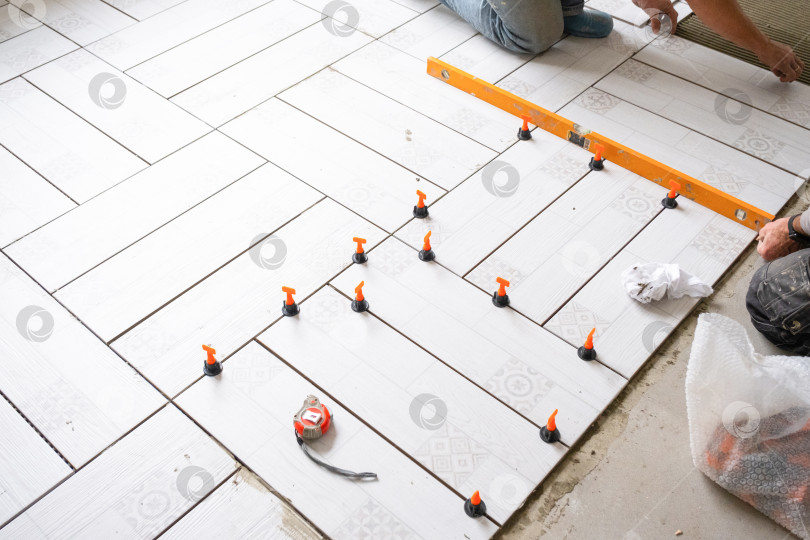 Скачать Укладка напольной плитки по диагонали, использование прокладок и уровня, текущий процесс укладки плитки, профессиональный ремонт, инструменты для точного выравнивания плитки. фотосток Ozero