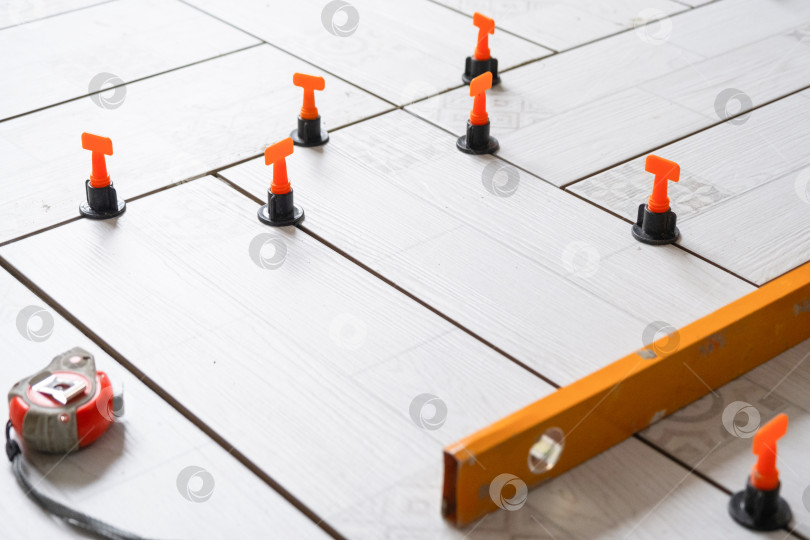 Скачать Ведется укладка плитки на пол, керамическая плитка с прокладками и системой выравнивания, ремонтные работы, обустройство дома, профессиональные инструменты для монтажа. фотосток Ozero