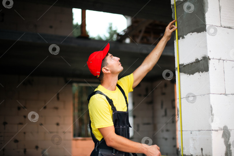 Скачать Строитель проверяет высоту оконного проема по вертикали, замеряет место установки, планирует перегородки, выполняет работы по реконструкции здания. фотосток Ozero