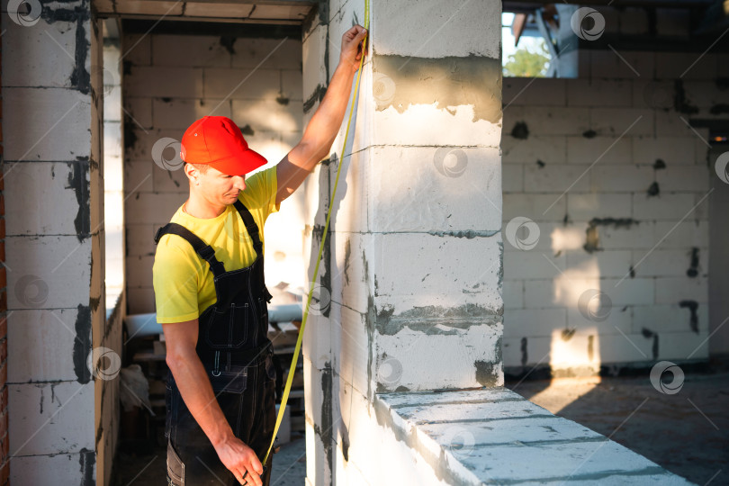 Скачать Рабочий измеряет высоту окна и стены для установки, перепланировки интерьера, разметки перегородки для установки окон и дверей, благоустройства и ремонта помещения. фотосток Ozero