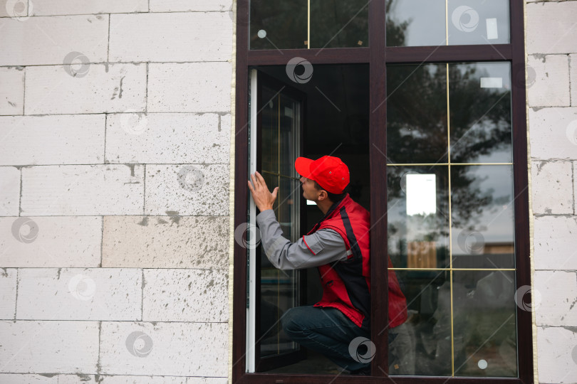 Скачать Рабочий регулирует только что установленное пластиковое окно в доме, обеспечивает герметизацию и выравнивание, контроль качества профессиональным установщиком окон, ремонт дома. фотосток Ozero