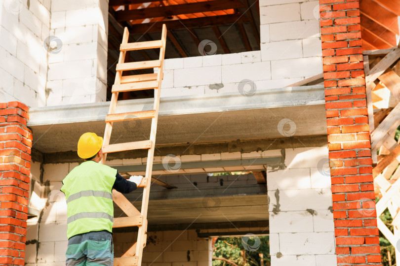 Скачать Строитель на строительной площадке, рабочий взбирается по лестнице, монтирует строительные леса, возводит конструкцию дома, меры безопасности, задачи строительного бизнеса. фотосток Ozero