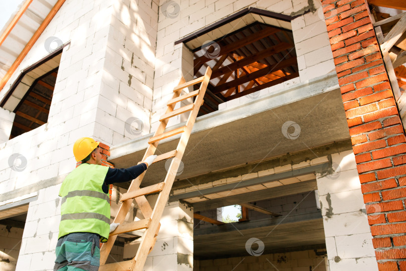 Скачать Строитель устанавливает лестницу для доступа на крышу, приступает к кладке, обустройству площадки, инструктажу по технике безопасности для команды, кладке кирпича, процессу строительства, проекту дома. фотосток Ozero