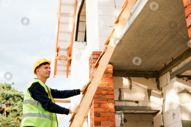 Скачать Специалист по строительству измеряет точки установки, выравнивает деревянную балку, защитный шлем, ход строительства, детали подгонки, организацию командной работы, профессиональный рабочий процесс. фотосток Ozero