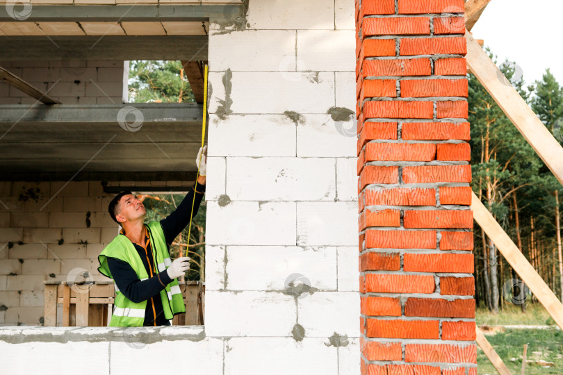 Скачать Застройщик измеряет оконный проем, отмечает линию монтажа, подготавливает кирпичную стену, строит совместно, настраивает площадку, проект дома, колонны, проверяет раму, улучшает качество. фотосток Ozero