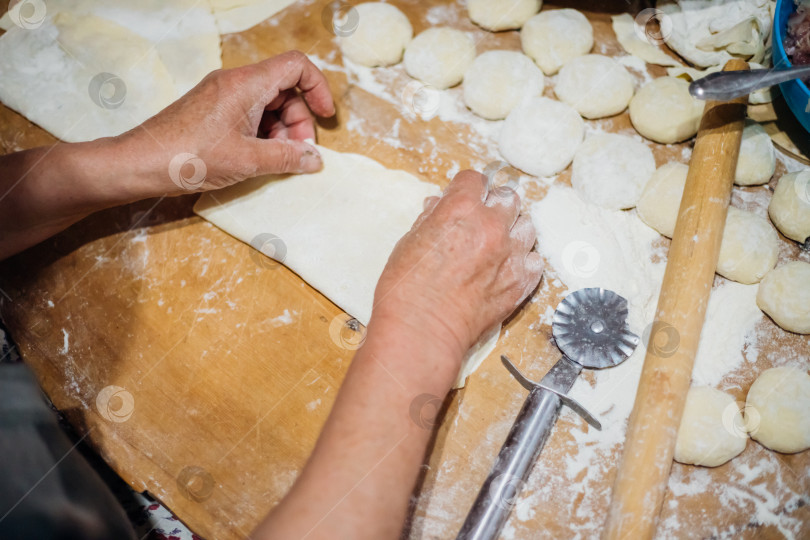 Скачать Крупный план женских рук пожилой женщины, раскатывающей тесто деревянной скалкой. Приготовление домашних пирогов и чебуреков. фотосток Ozero