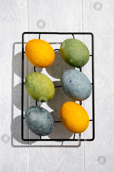 Скачать Пасхальные яйца, окрашенные естественным образом гибискусом и куркумой, сохнут на решетке для охлаждения, создавая красивую палитру желтых и зеленых оттенков, готовые к празднованию Пасхи фотосток Ozero