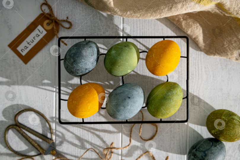 Скачать Пасхальные яйца, окрашенные естественным образом гибискусом и куркумой, сохнут на решетке для охлаждения, создавая красивую палитру желтых и зеленых оттенков, готовые к празднованию Пасхи фотосток Ozero