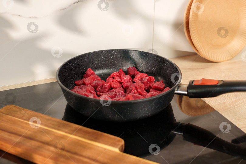 Скачать Готовьте говяжьи кубики на современной кухне на плите, рядом с которой находится деревянная посуда фотосток Ozero