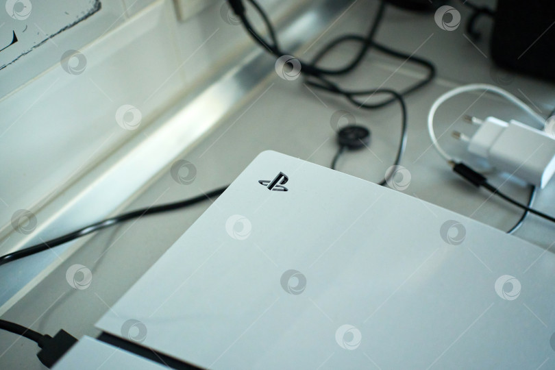 Скачать Тюмень, Россия - 8 июля 2025 года: Элегантная игровая консоль Sony PlayStation 5 установлена на современной поверхности и дополнена стильным контроллером, подключенным для зарядки фотосток Ozero
