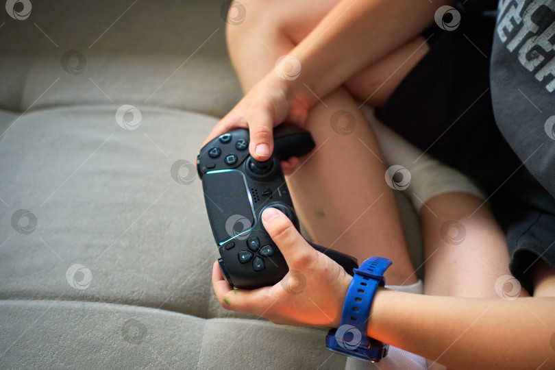 Скачать Тюмень, Россия - 8 июля 2025 года: Sony PlayStation 5 Молодой геймер удобно устроился в кресле, сосредоточенный на игре в свою любимую игру фотосток Ozero