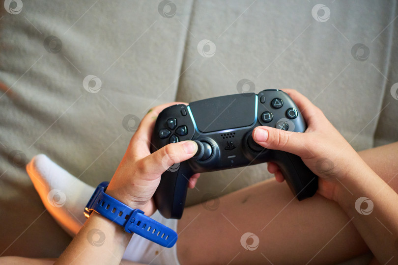 Скачать Тюмень, Россия - 8 июля 2025 года: Sony PlayStation 5 Молодой геймер удобно устроился в кресле, сосредоточенный на игре в свою любимую игру фотосток Ozero