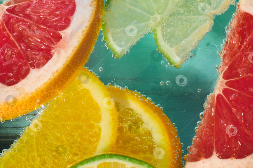 Скачать Яркие ломтики грейпфрута, лайма, лимона и апельсина погружаются в газированную воду, создавая яркий аромат. фотосток Ozero