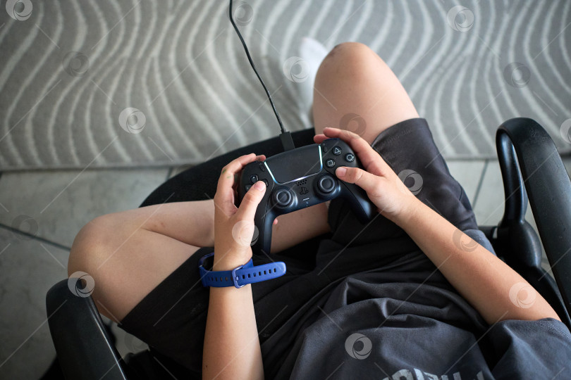 Скачать Тюмень, Россия - 8 июля 2025 года: Ребенок на Sony PlayStation 5 днем играет дома с консольным контроллером. фотосток Ozero