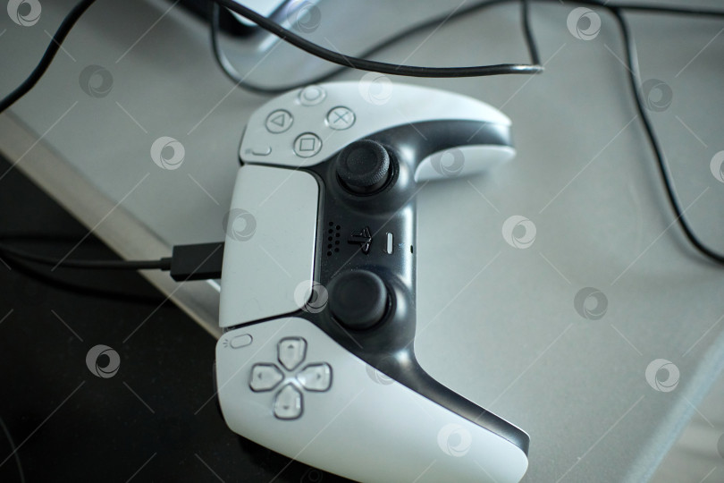 Скачать Тюмень, Россия - 8 июля 2025 года: Элегантная игровая консоль Sony PlayStation 5 установлена на современной поверхности и дополнена стильным контроллером, подключенным для зарядки фотосток Ozero