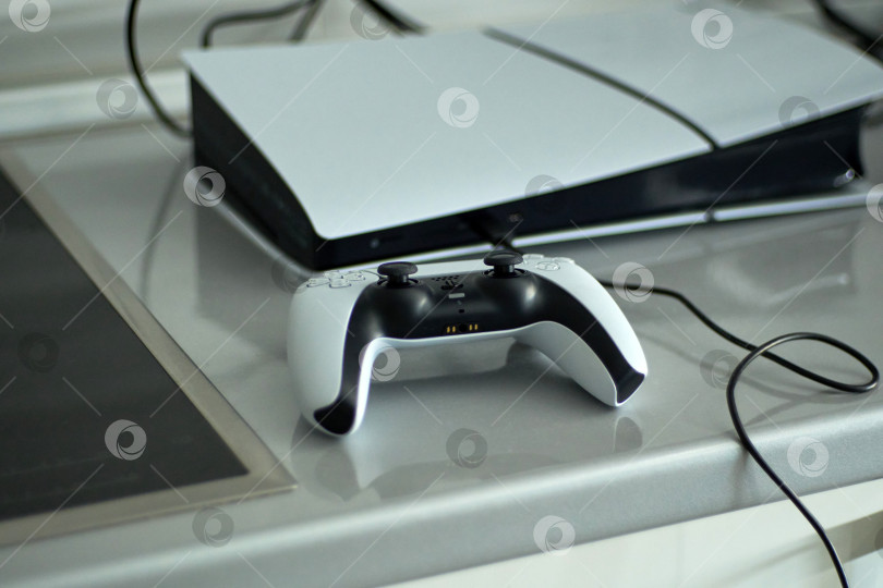 Скачать Тюмень, Россия - 8 июля 2025 года: Консоль Sony PlayStation 5 демонстрирует игровую систему нового поколения с контроллером на зарядной станции. фотосток Ozero