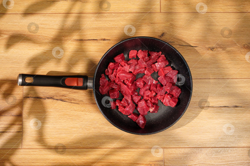 Скачать Свежая говядина, нарезанная кубиками, готовится на сковороде на деревянной поверхности при естественном освещении. фотосток Ozero