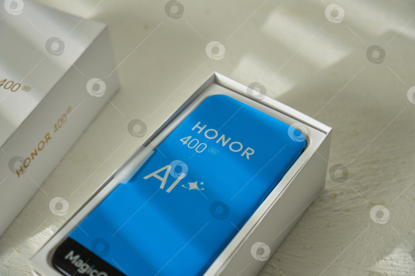 Скачать Тюмень, Россия - 15 августа 2025 года: Новый смартфон Honor 400 представлен в стильной упаковке в домашней обстановке с естественным освещением. фотосток Ozero