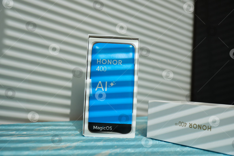 Скачать Тюмень, Россия - 15 августа 2025 года: Новый смартфон Honor 400 представлен в стильной упаковке в домашней обстановке с естественным освещением. фотосток Ozero