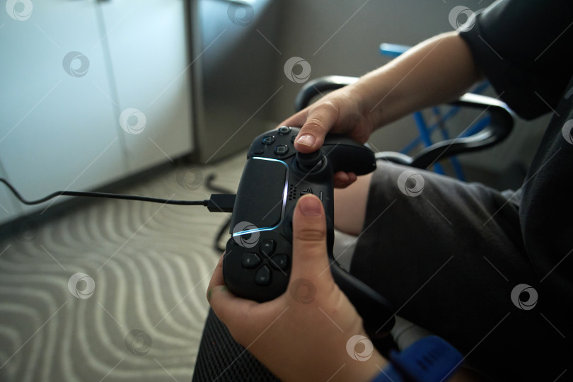 Скачать Тюмень, Россия - 8 июля 2025 года: Sony PlayStation 5 Молодой геймер удобно устроился в кресле, сосредоточенный на игре в свою любимую игру фотосток Ozero