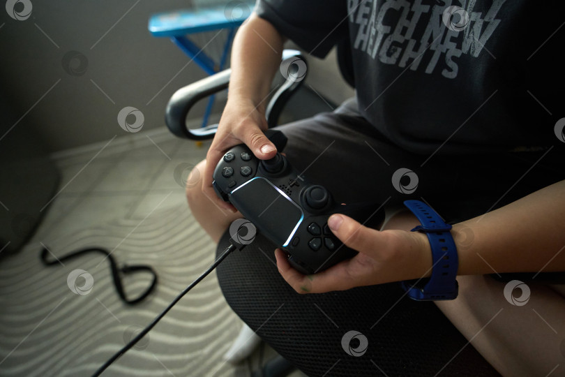 Скачать Тюмень, Россия - 8 июля 2025 года: Пользователь Sony PlayStation 5 работает с игровым контроллером, сидя в современной комнате в дневное время фотосток Ozero