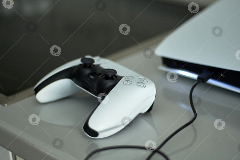 Скачать Тюмень, Россия - 8 июля 2025 года: Консоль Sony PlayStation 5 демонстрирует игровую систему нового поколения с контроллером на зарядной станции. фотосток Ozero