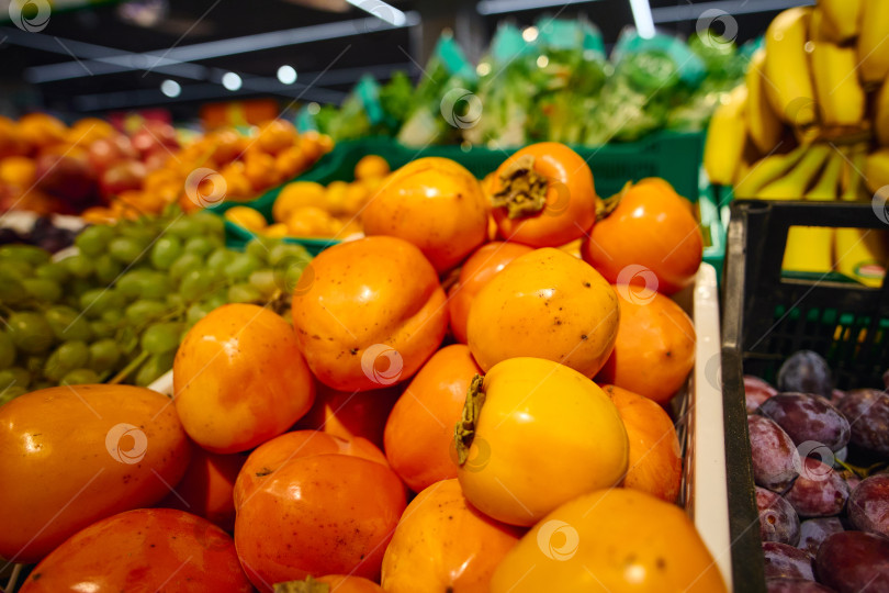 Скачать Свежая хурма среди различных фруктов в продуктовом отделе продуктового магазина в дневное время фотосток Ozero