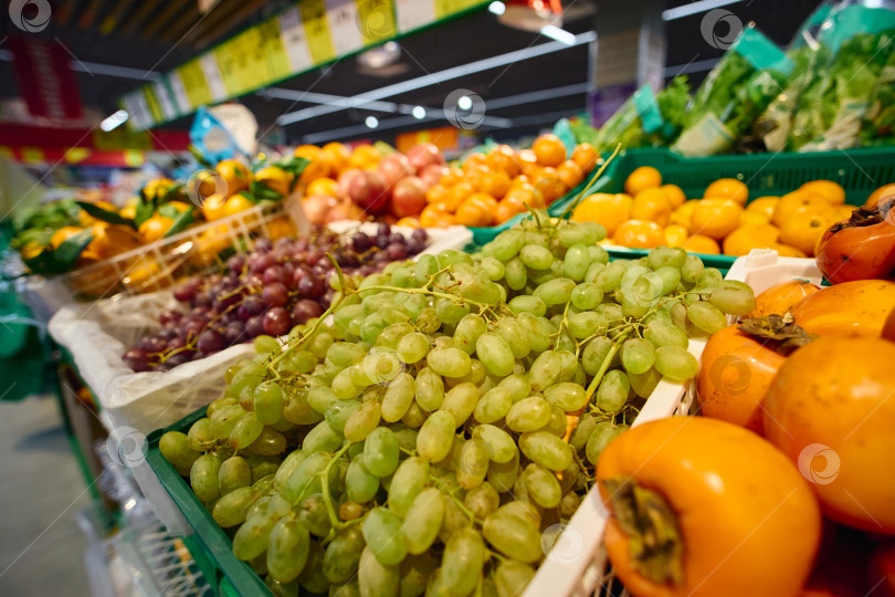Скачать В продуктовом магазине выставлены корзины со свежими фруктами. На сцене изображены зеленый виноград и апельсины. фотосток Ozero