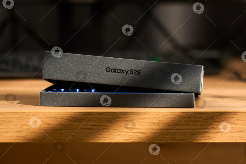 Скачать Тюмень, Россия - 3 декабря 2025 года: Новый смартфон samsung s25 лежит рядом со своей коробкой на деревянной поверхности, на которой четко видны основные детали фотосток Ozero
