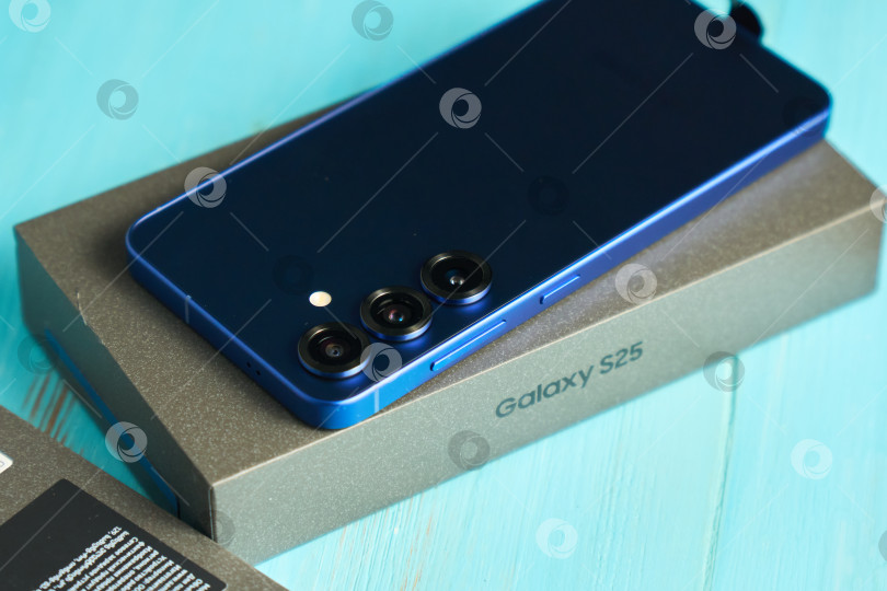 Скачать Тюмень, Россия - 3 декабря 2025 г.: Samsung S25, размещенный на деревянном столе в светлой комнате, демонстрирует свой элегантный дизайн и функции камеры. фотосток Ozero