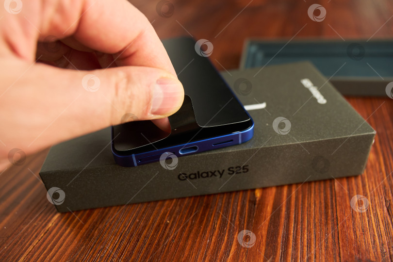 Скачать Тюмень, Россия - 3 декабря 2025 г.: Samsung S25, размещенный на деревянном столе в светлой комнате, демонстрирует свой элегантный дизайн и функции камеры. фотосток Ozero