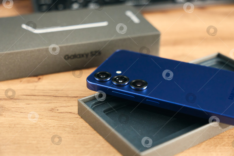 Скачать Тюмень, Россия - 3 декабря 2025 г.: Samsung S25, размещенный на деревянном столе в светлой комнате, демонстрирует свой элегантный дизайн и функции камеры. фотосток Ozero