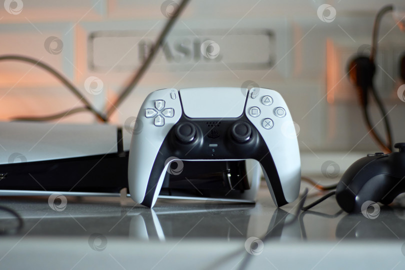 Скачать Тюмень, Россия - 8 июля 2025 года: Консоль Sony PlayStation 5 демонстрирует игровую систему нового поколения с контроллером на зарядной станции. фотосток Ozero