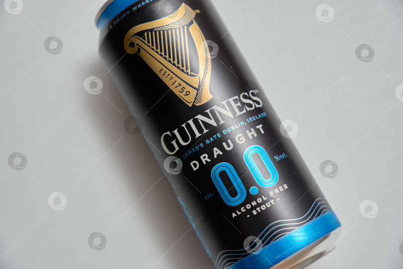 Скачать Тюмень, Россия - 11 декабря 2025 г.: Банка безалкогольного пива guinness стоит на синем покрывале. Банка оформлена в темном стиле и содержит информацию фотосток Ozero