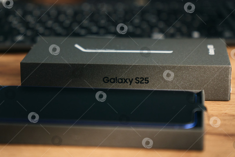 Скачать Тюмень, Россия - 3 декабря 2025 г.: Samsung S25, размещенный на деревянном столе в светлой комнате, демонстрирует свой элегантный дизайн и функции камеры. фотосток Ozero