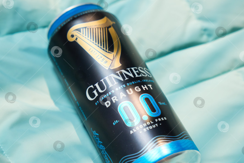 Скачать Тюмень, Россия - 11 декабря 2025 г.: Банка безалкогольного пива guinness стоит на синем покрывале. Банка оформлена в темном стиле и содержит информацию фотосток Ozero